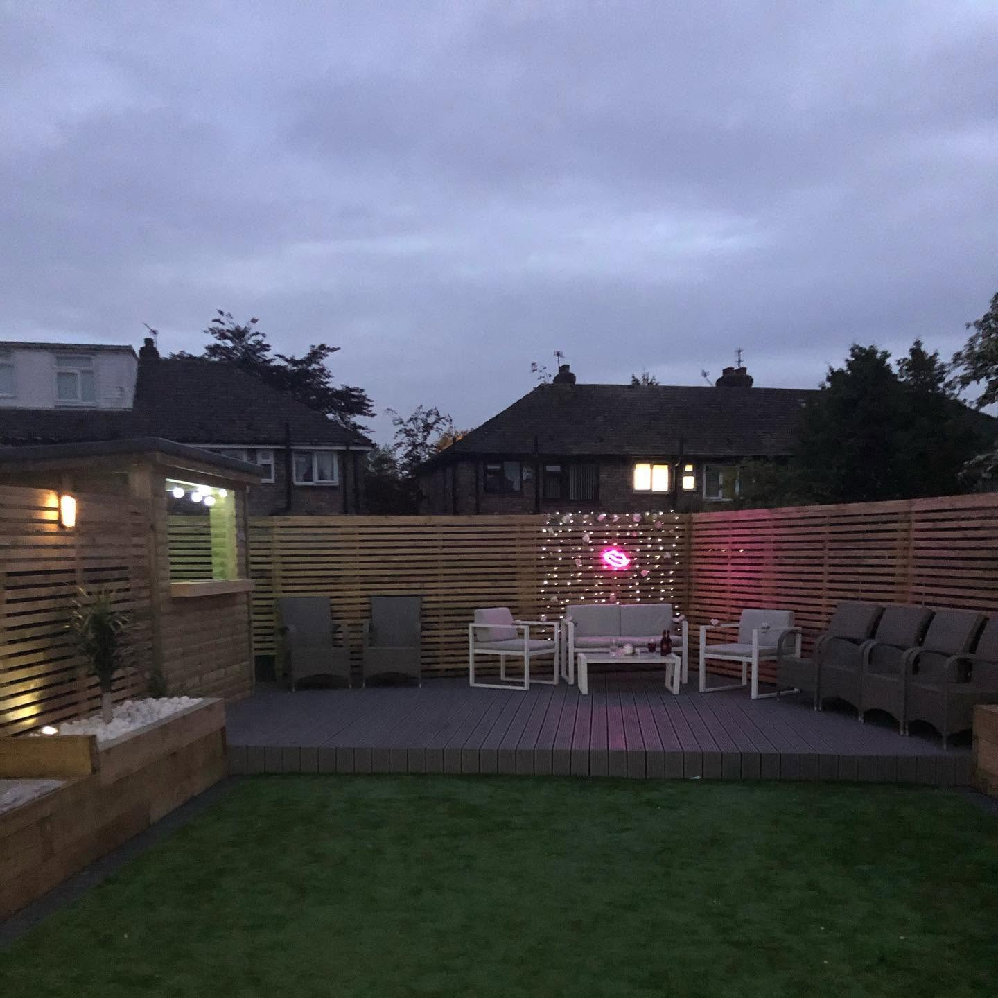 Same garden after RG landscaping — composite decking, bespoke bar, slatted screens and new lawn at twilight